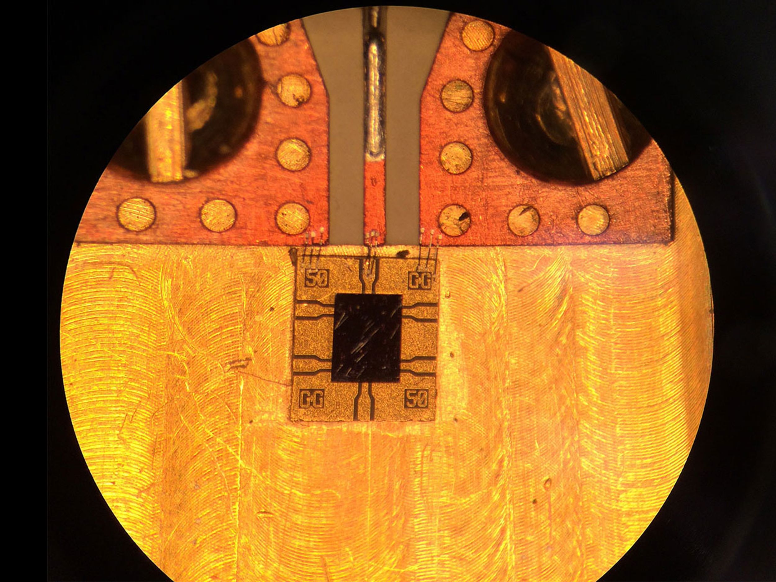 A high-speed, semiconductor photodiode (black rectangle) with a diode surrounded by a gold-coated border in which electrical leads are embedded. Wires connect the leads to the copper electrical circuit (top).