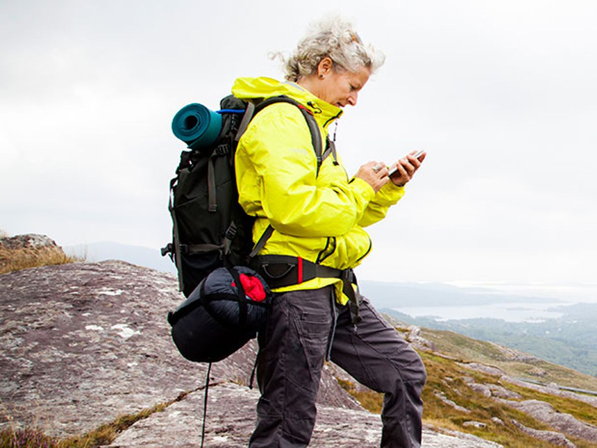 A hiker in a yellow jack looks at her smartphone.