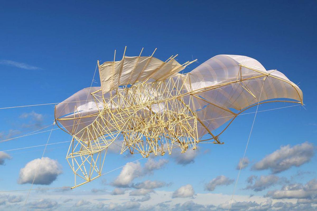 A huge kite with sails and mechanical limbs soars in a blue sky