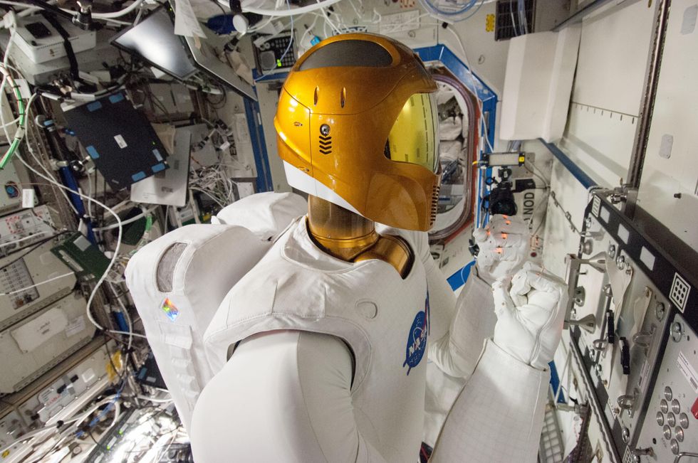 A human-sized white humanoid robot with a golden helmet and visor, in front of a task board on the International Space Station