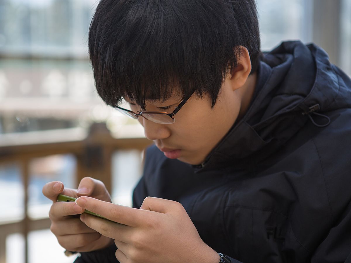 A Korean teenager staring intently at a smartphone.