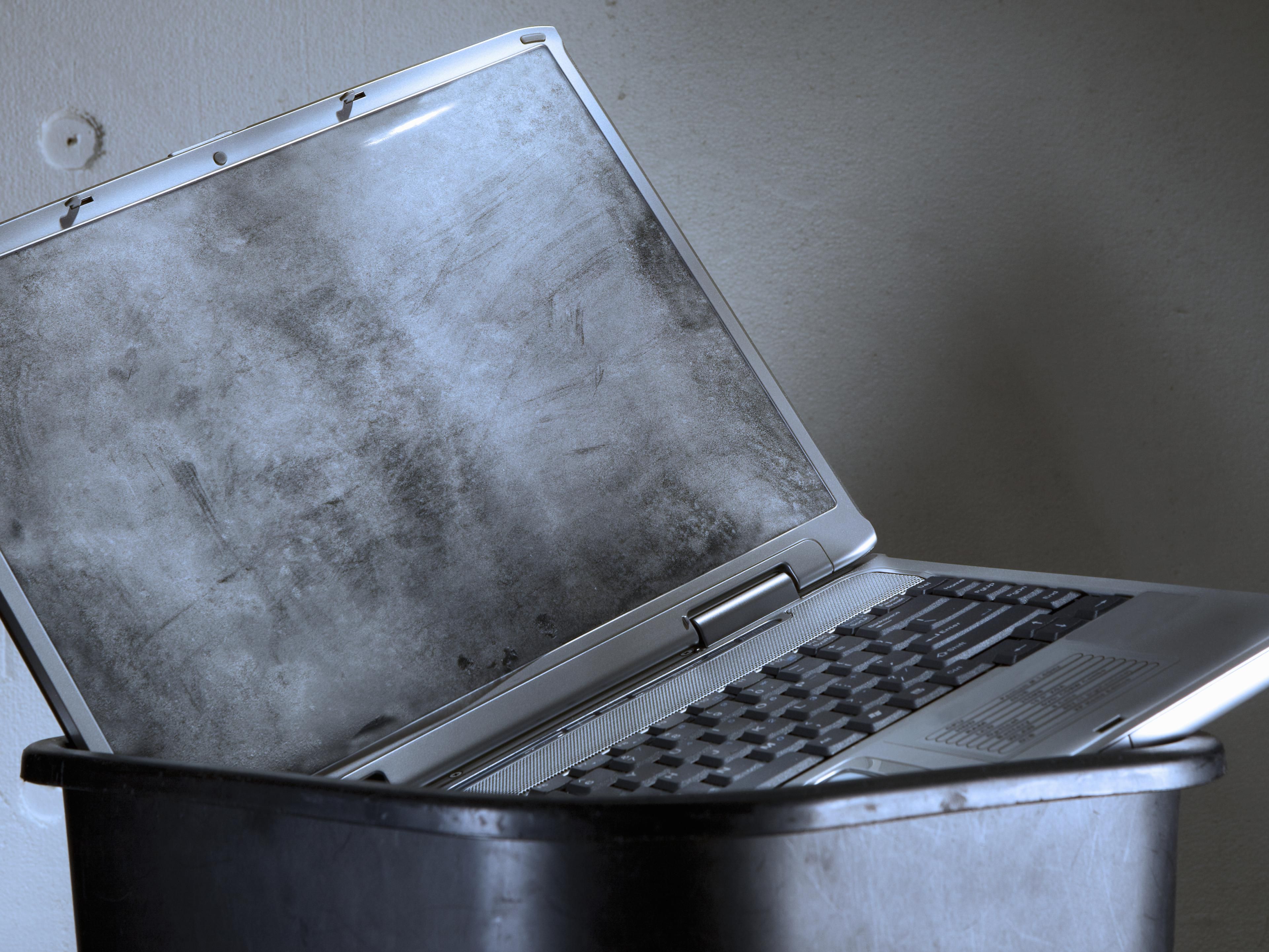 A laptop computer sits in a garbage pail.