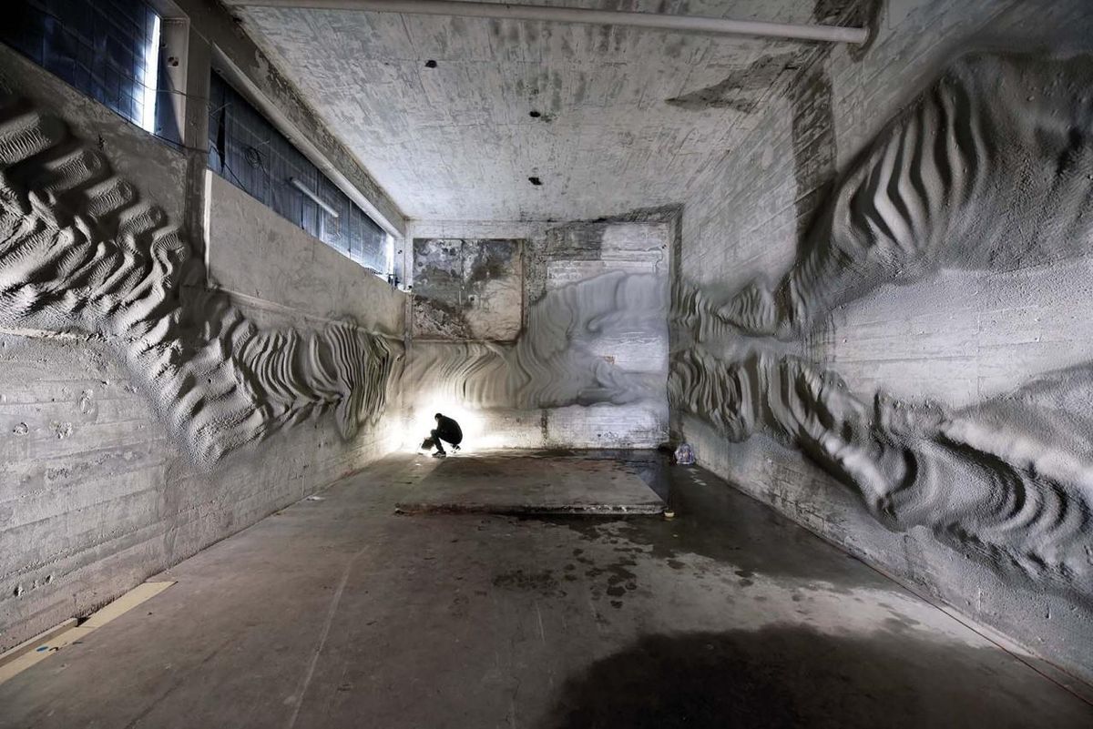 A large concrete room with intricate, flowing 3D designs made of plaster covering the walls