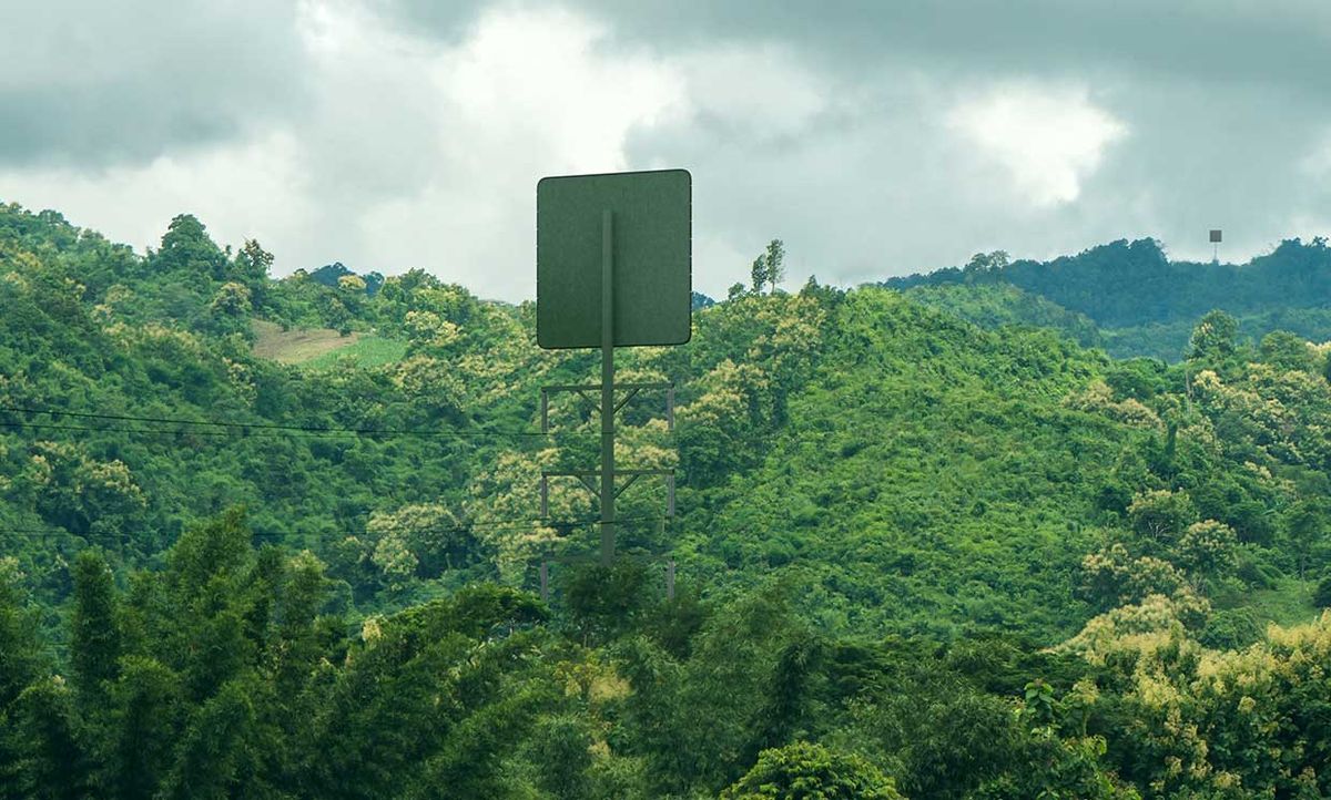 A large square panel is located atop a tall pole into a hilly area dense with vegetation. On a distant hill, another square panel atop a pole can be seen.