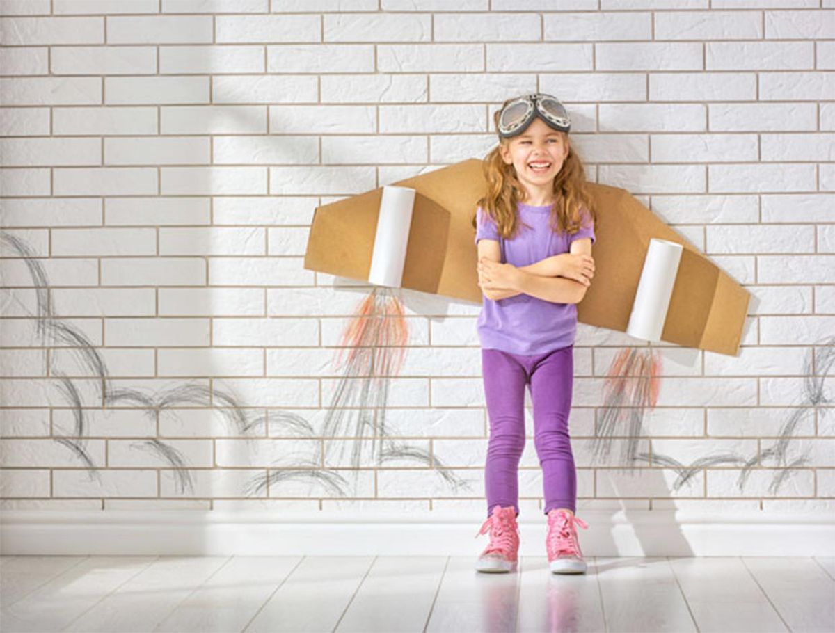 A little girl with cardboard wings and googles on her head.  