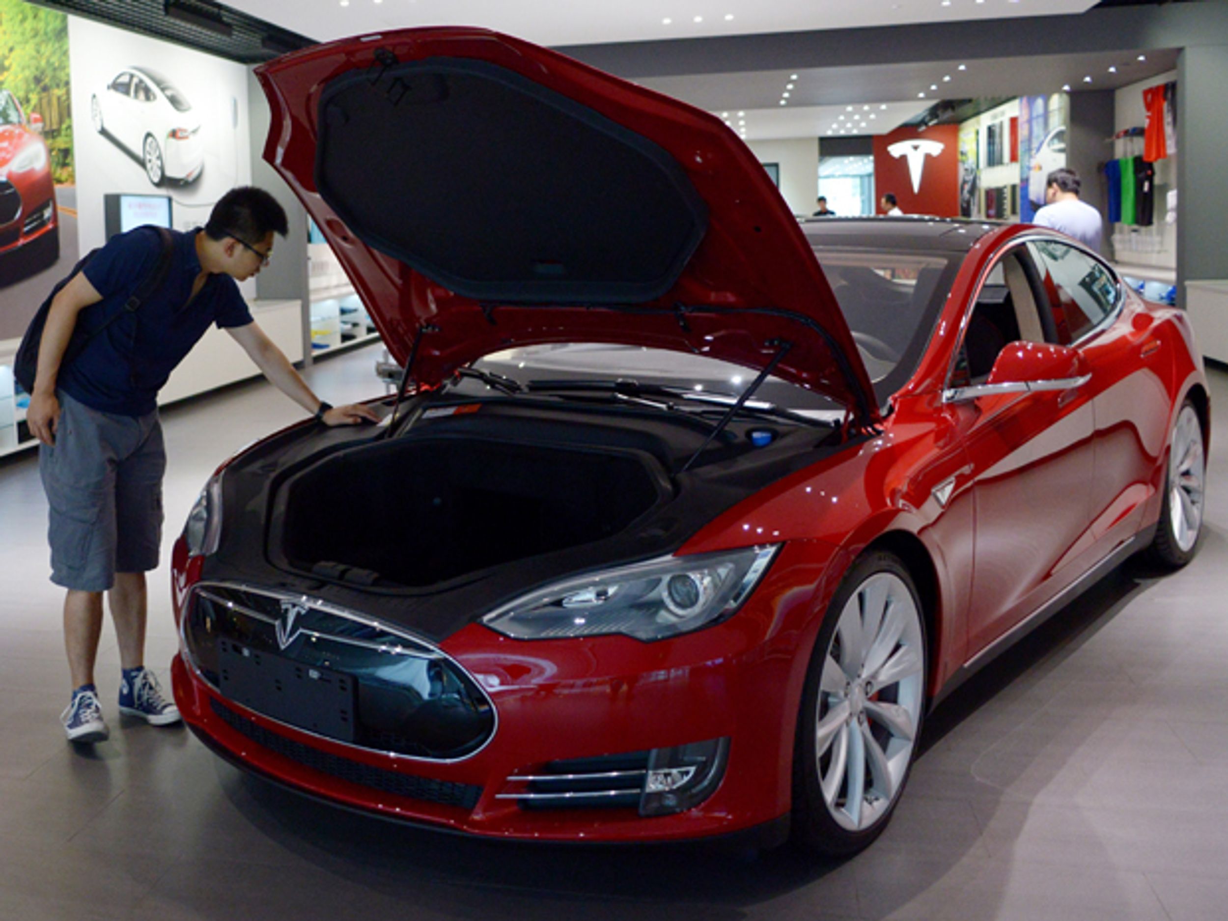 A man checks out the engine of a red Tesla car