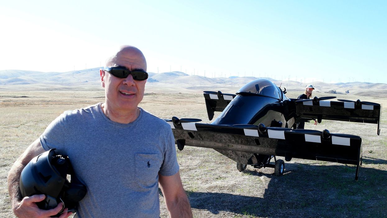 I Fly Opener’s BlackFly eVTOL | Tech Do a man holding a helmet stands in front of a black evtol in an empty landscape