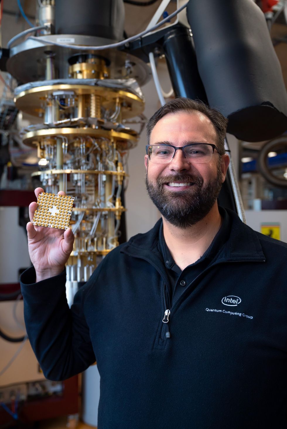 A man holds a bumpy gold rectangle in front of a spindly machine.