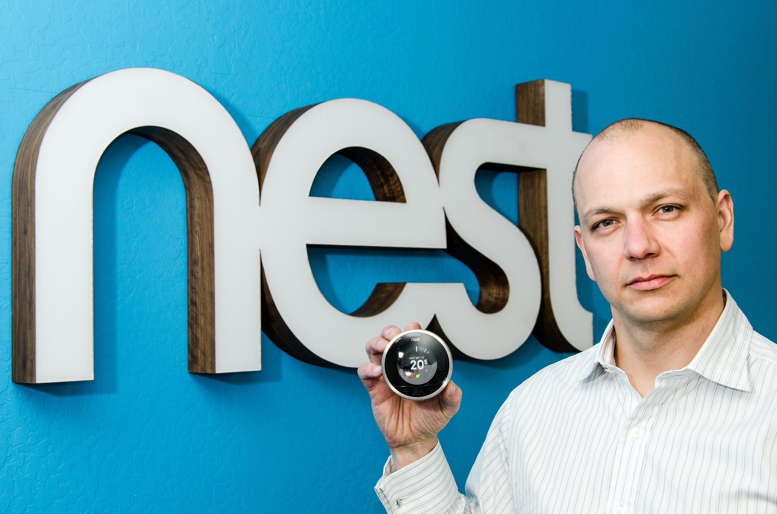 A man holds a circular device in front of a blue wall that says nest on it.