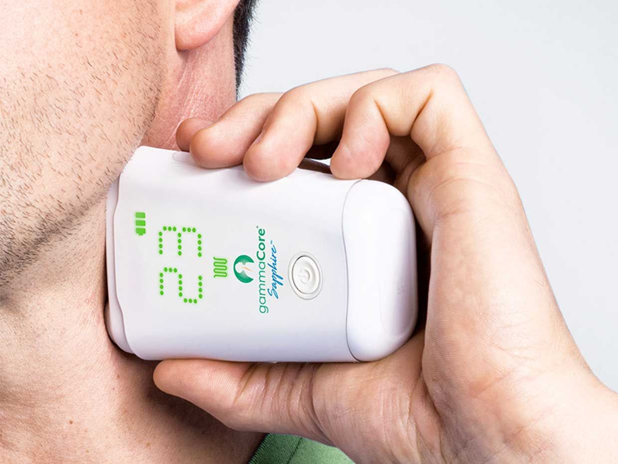 A man holds the gammaCore Sapphire CV, a non-invasive vagus nerve stimulator, up to his neck.