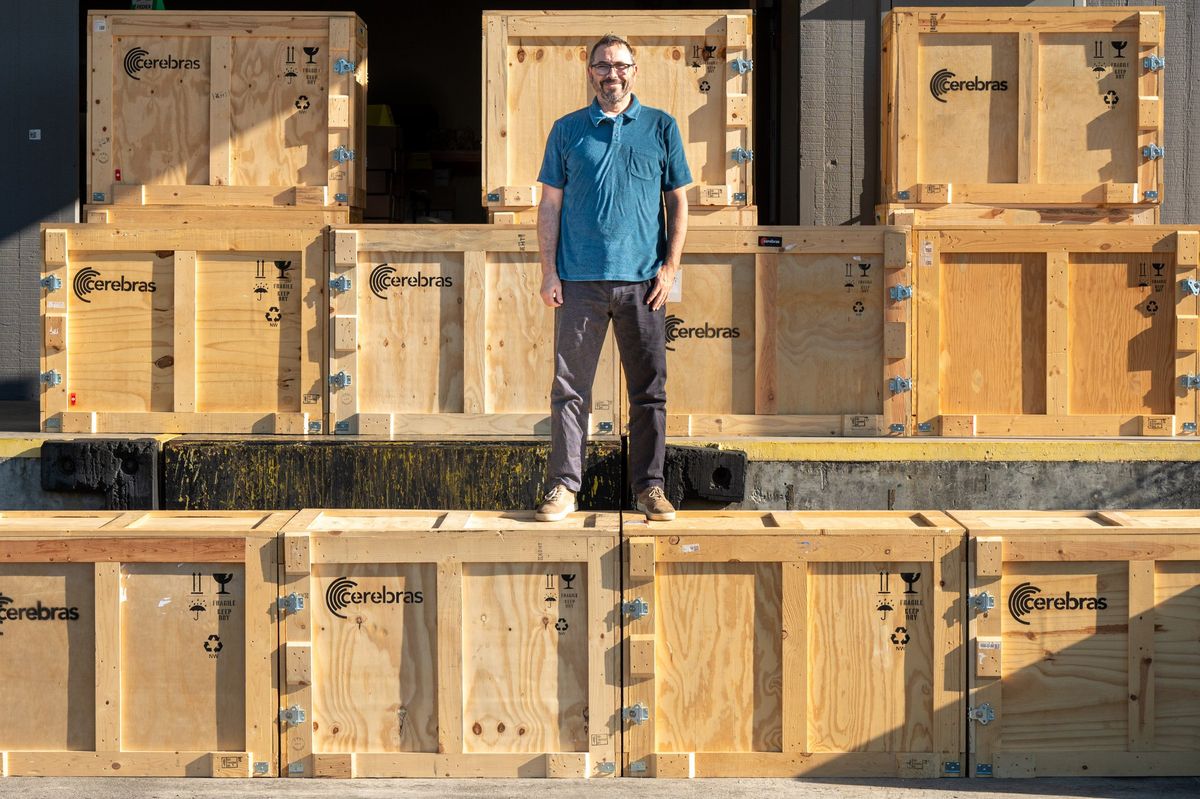 A man in a blue short-sleeve shirt stands atop and among crates marked 'Cerebras'.