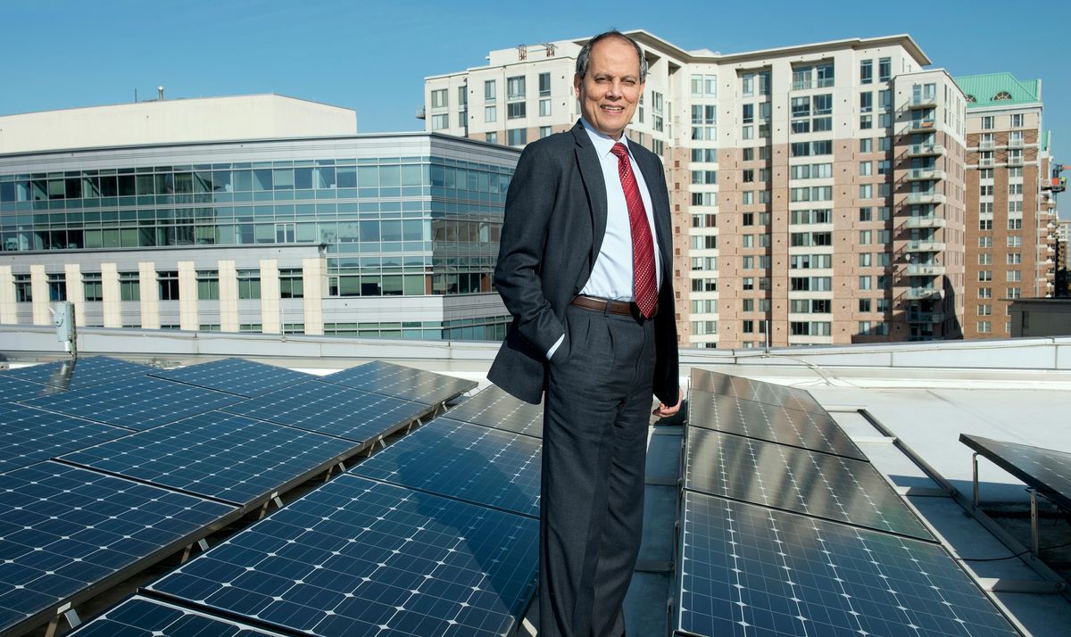 A man in a suit stands amidst a rooftop solar installation, with buildings behind him.