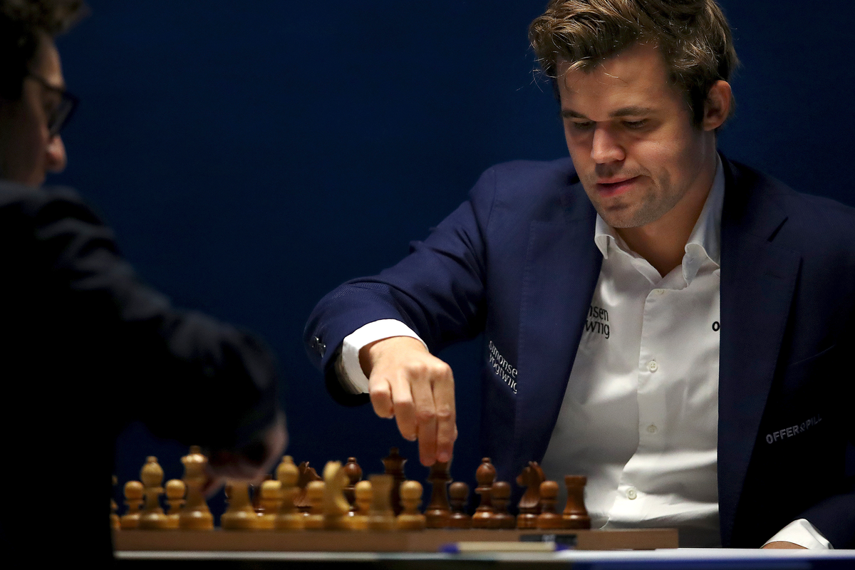 A man in a white shirt and blue blazer moves a chess piece on a board.