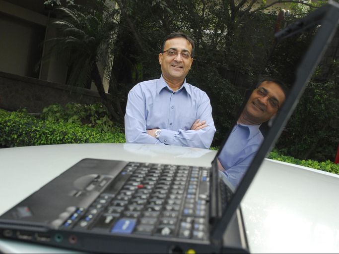 A man in glasses smiles at the camera. In the foreground is a computer. Info for editor if needed: Ajay Bhatt, Chief Platform Architect at Mobile Platform Group, Intel Corporation poses for a profile shoot on January 20, 2010 in New Delhi, India.
