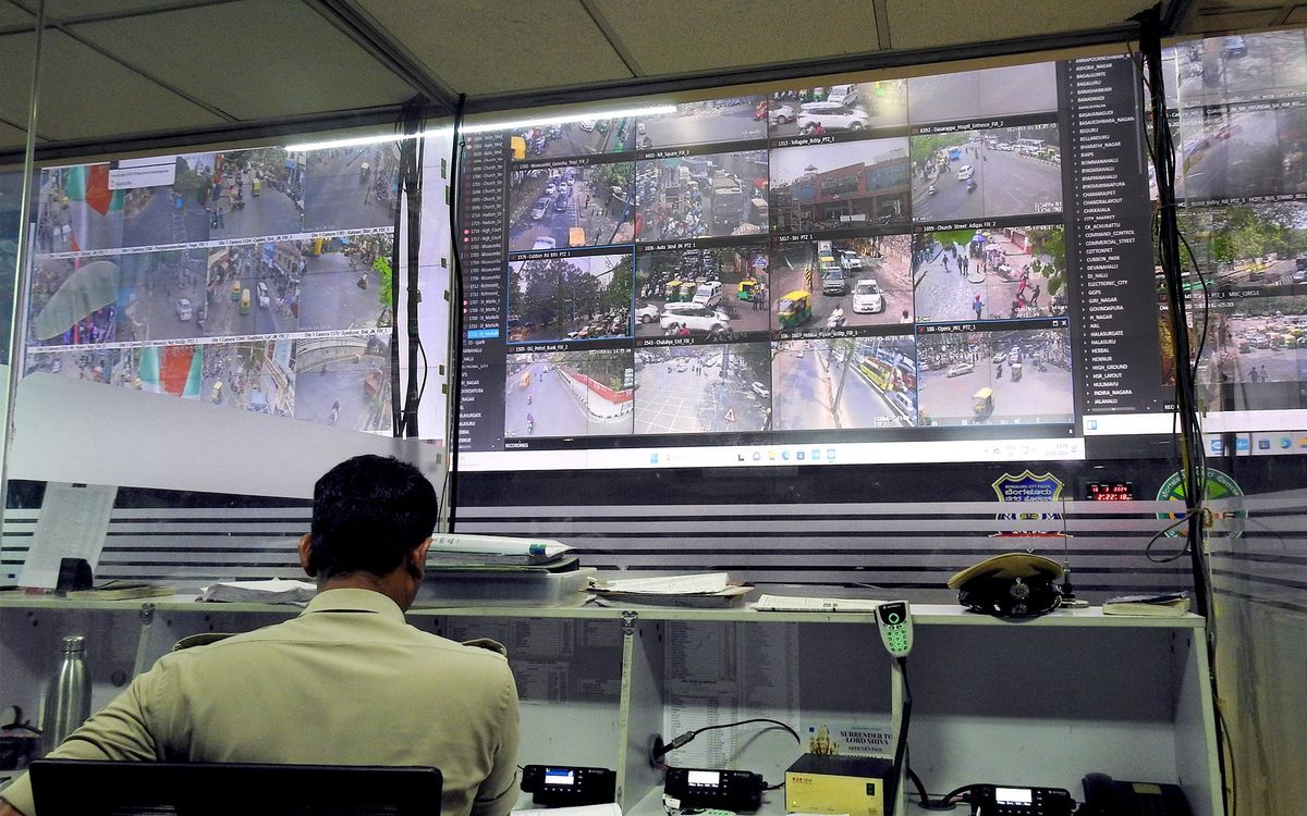 A man is seen from behind at a desk in front of three jumbo screens with the feeds from many traffic cameras.