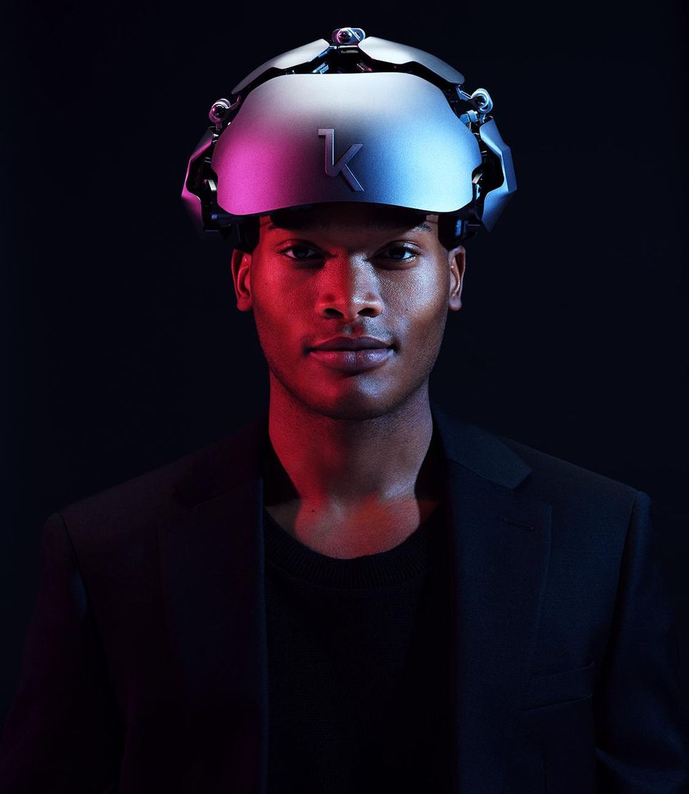 A man is wearing a silver device that looks like a helmet on his head. The front of the device is marked with a K.u00a0