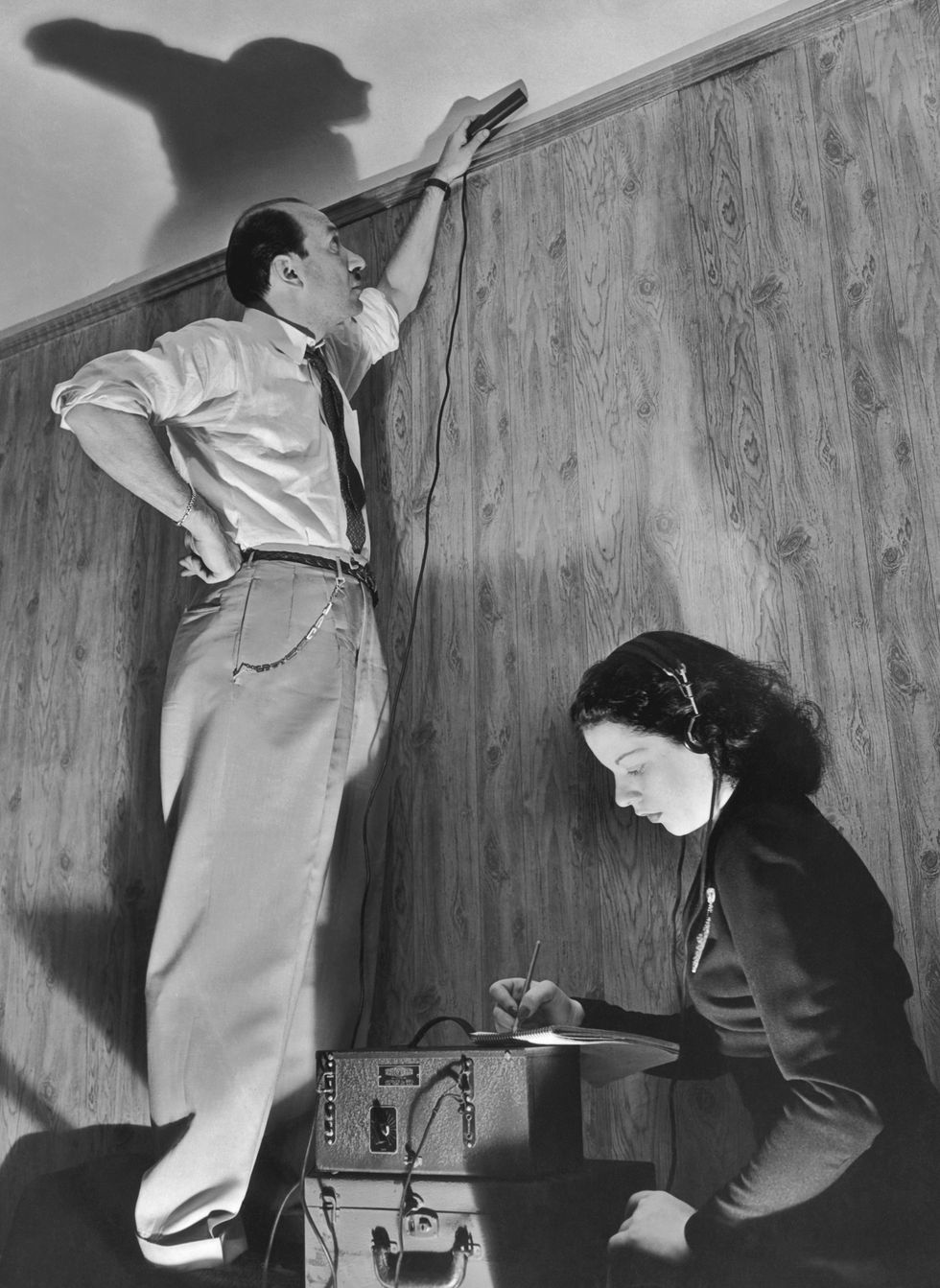A man places an electronic device near a wire while a woman operates recording gear.