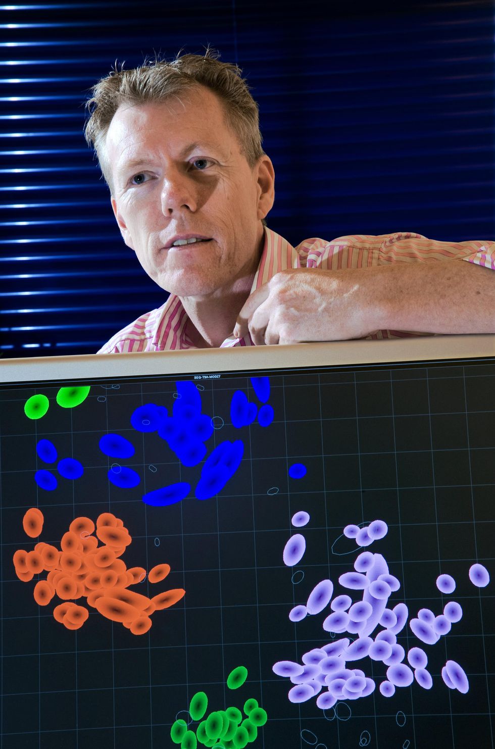 A man rests his arm on the top of computer screen showing clusters of colorful circles on a back background.