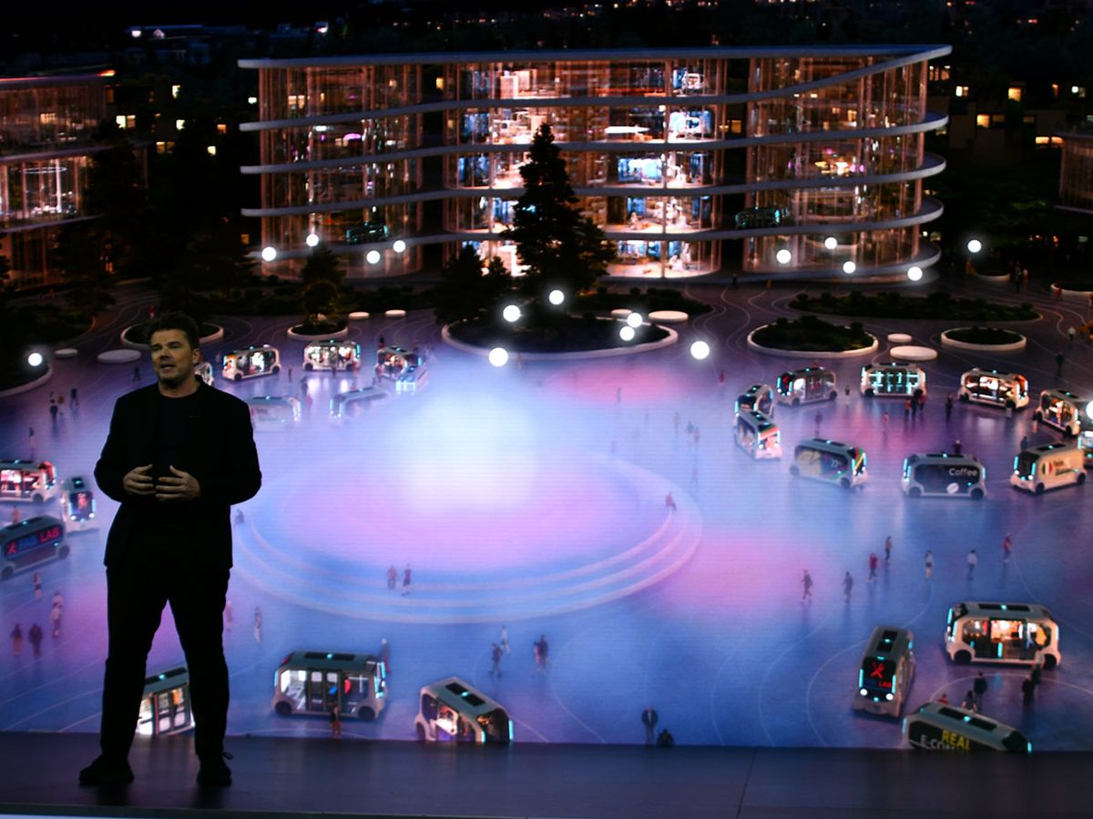 A man stands in front of a colorful rendering of passengers and self-driving cars in Toyota's Woven City.