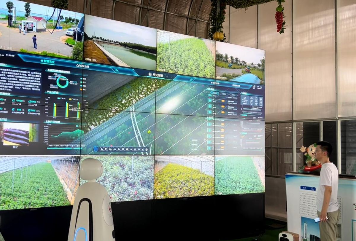A man stands in front of a giant screen made of 16 monitors, each showing agriculture and data as well as some text in Chinese.