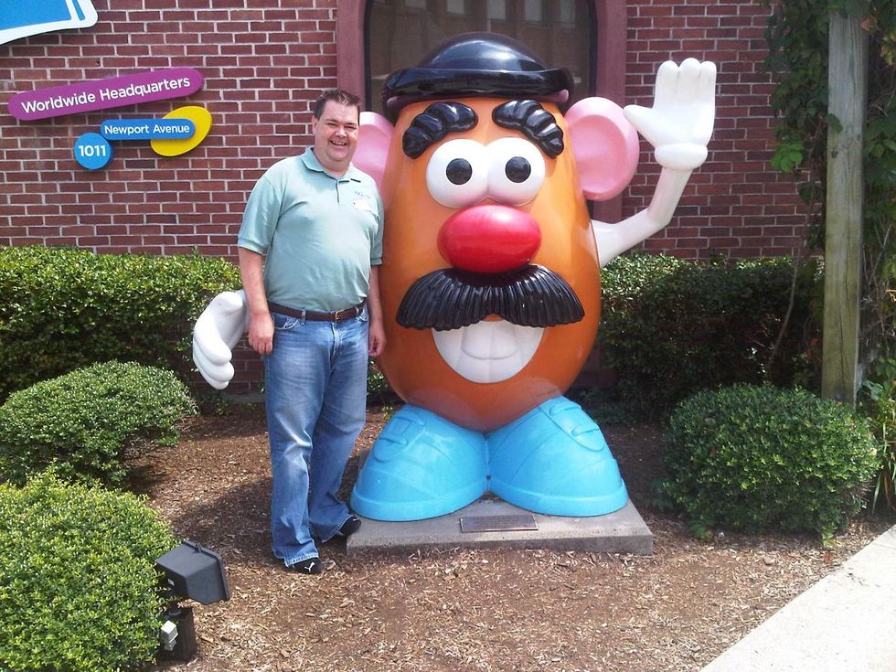 A man stands next to a statue of Mr. Potato Head