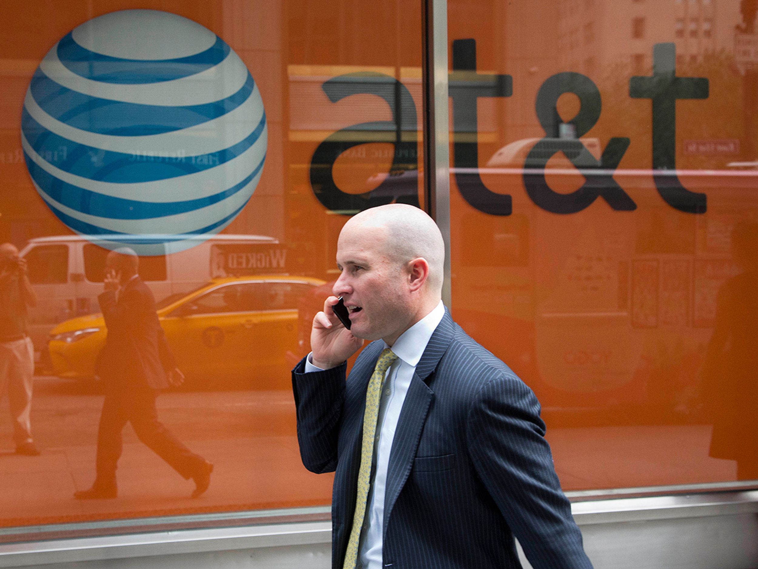 A man using a mobile phone walks past an AT&T store in New York.