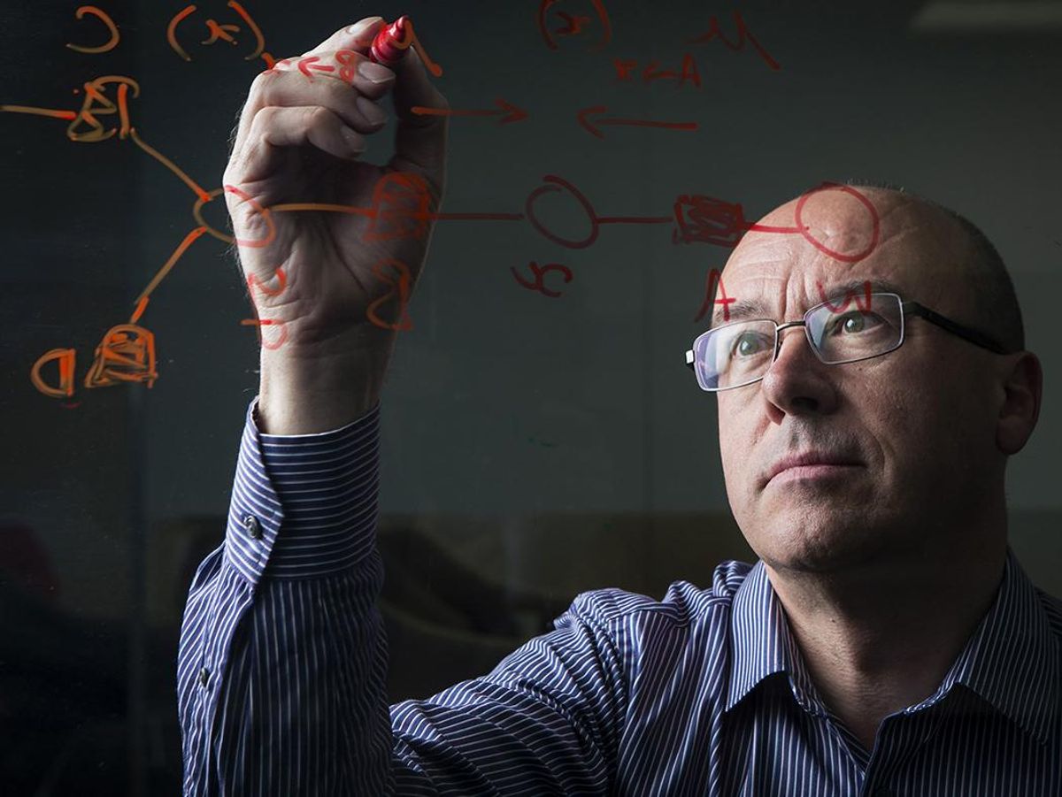 A man wearing glasses writes scientific formulas on glass.