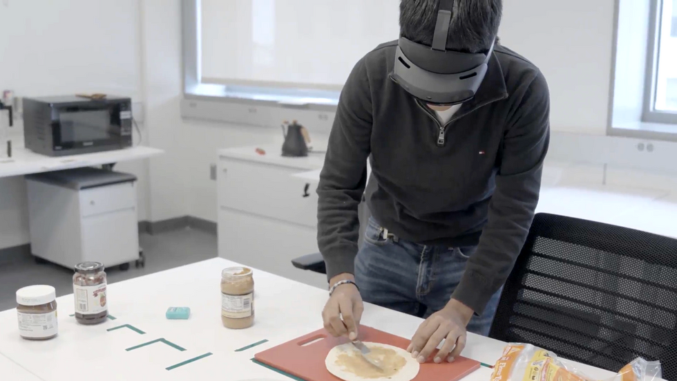 A man wearing VR googles spreads nut butter on a tortilla as part of an experiment in a test kitchen lab.