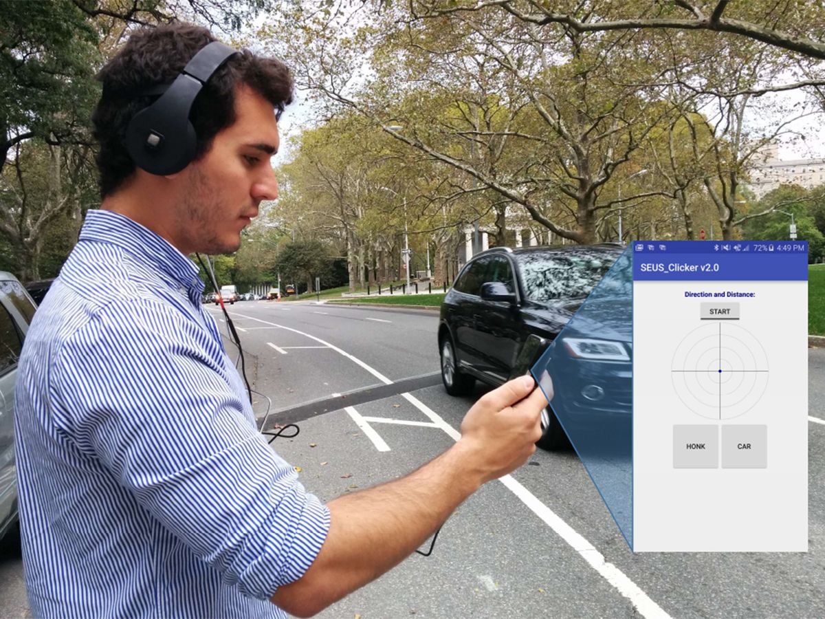 A man wears headphones and look at a screen in front of him while a car passes on a nearby street.