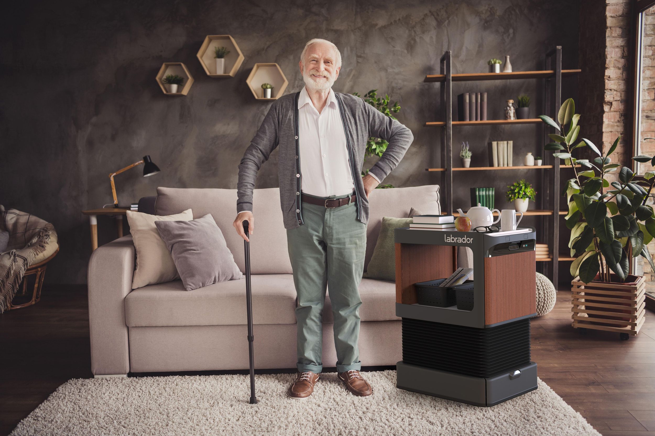 A man with a cane stands next to a robotic table in a living room.