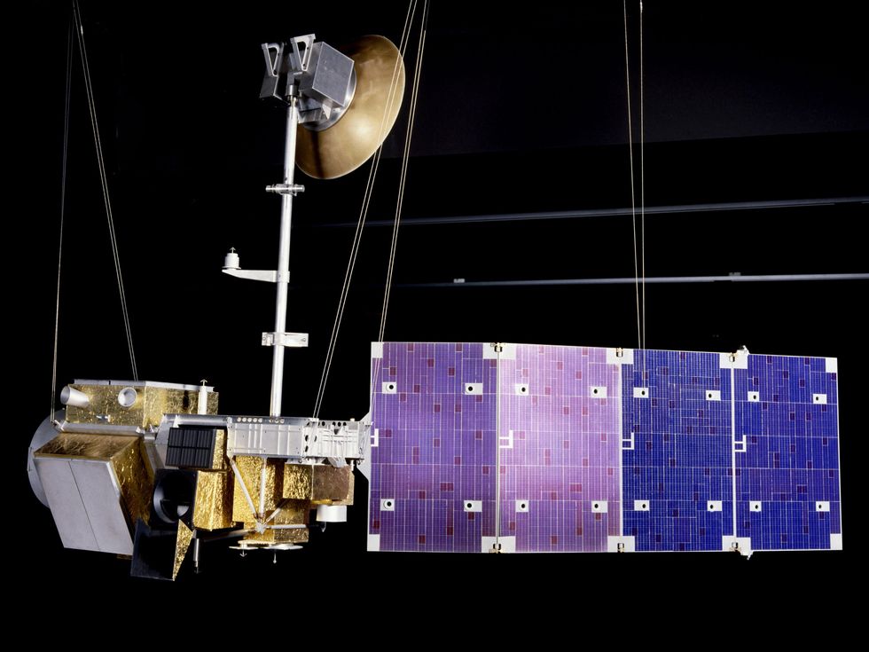 A model of a satellite that's suspended from wires and has solar panels, instrumentation, and other equipment extending from its body.