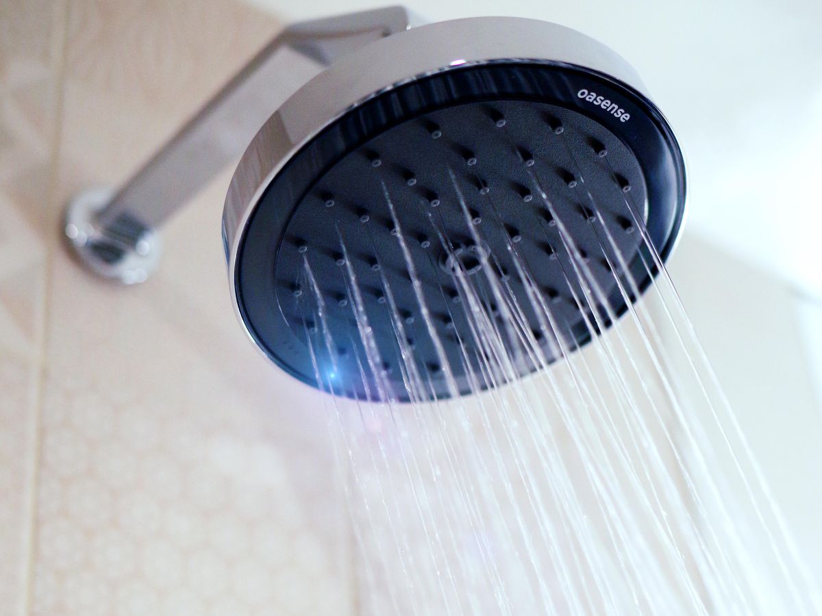 A mounted and running showerhead that says oasense and has a blue light on it.