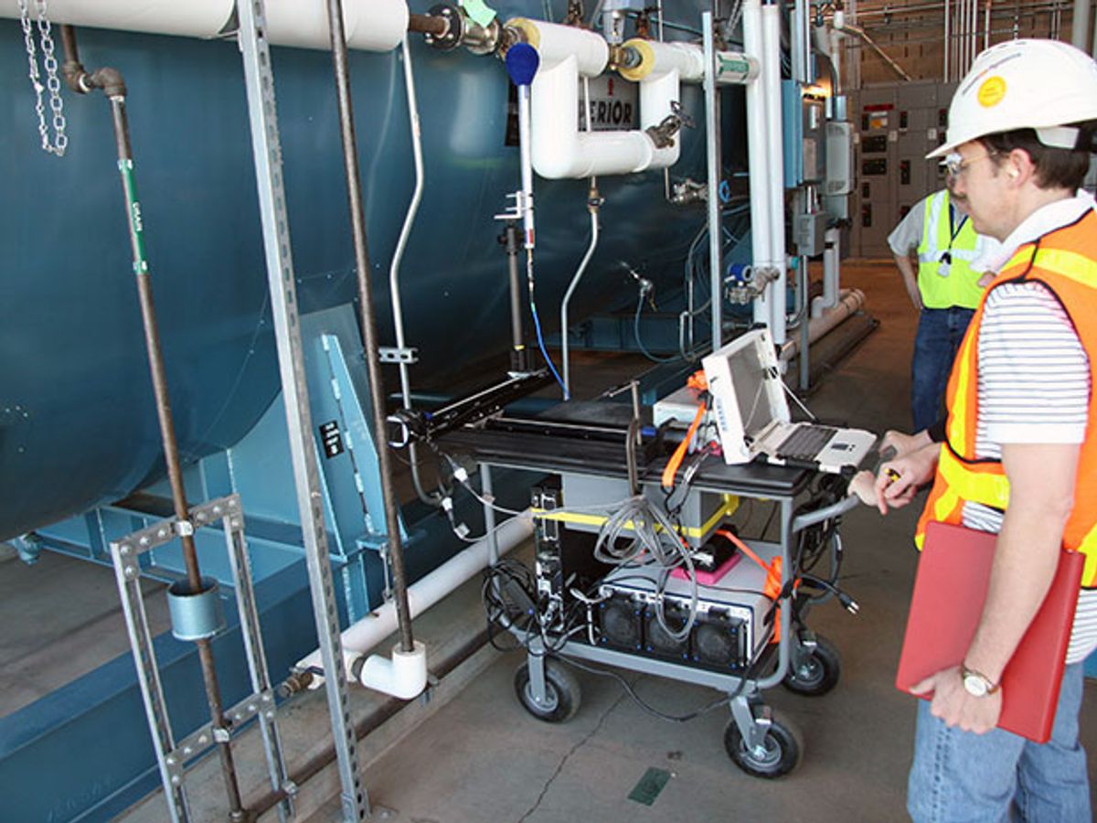 A NIST employee in a safety vest examines a wireless experiment inside of a steam generation plant.