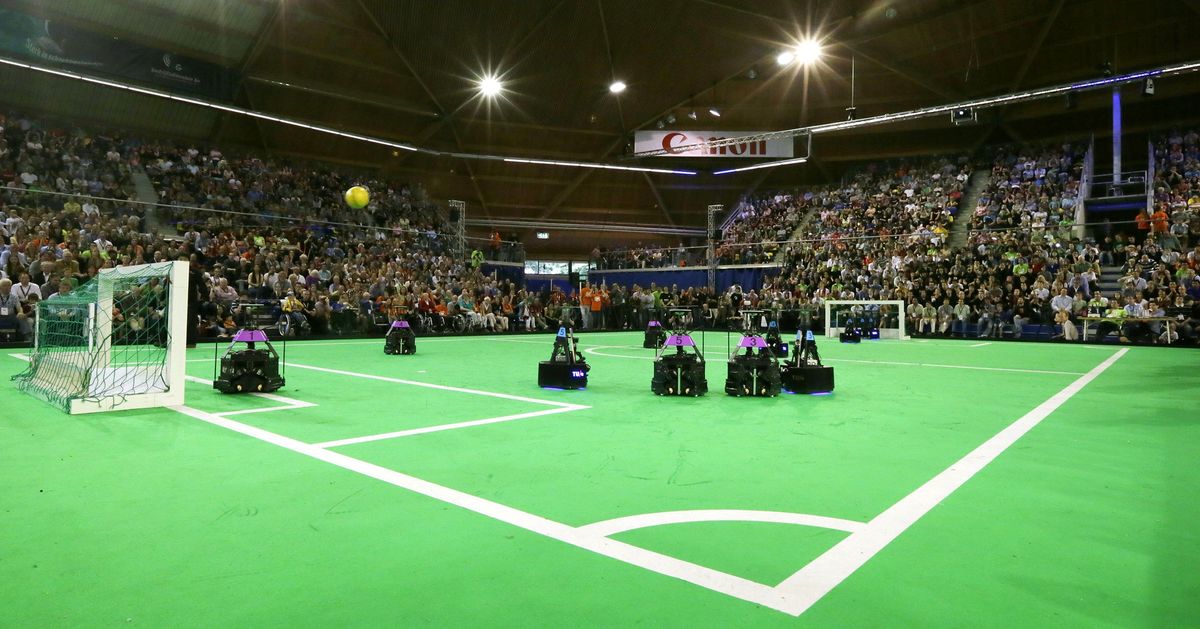 A number of small robots on a field in a stadium.