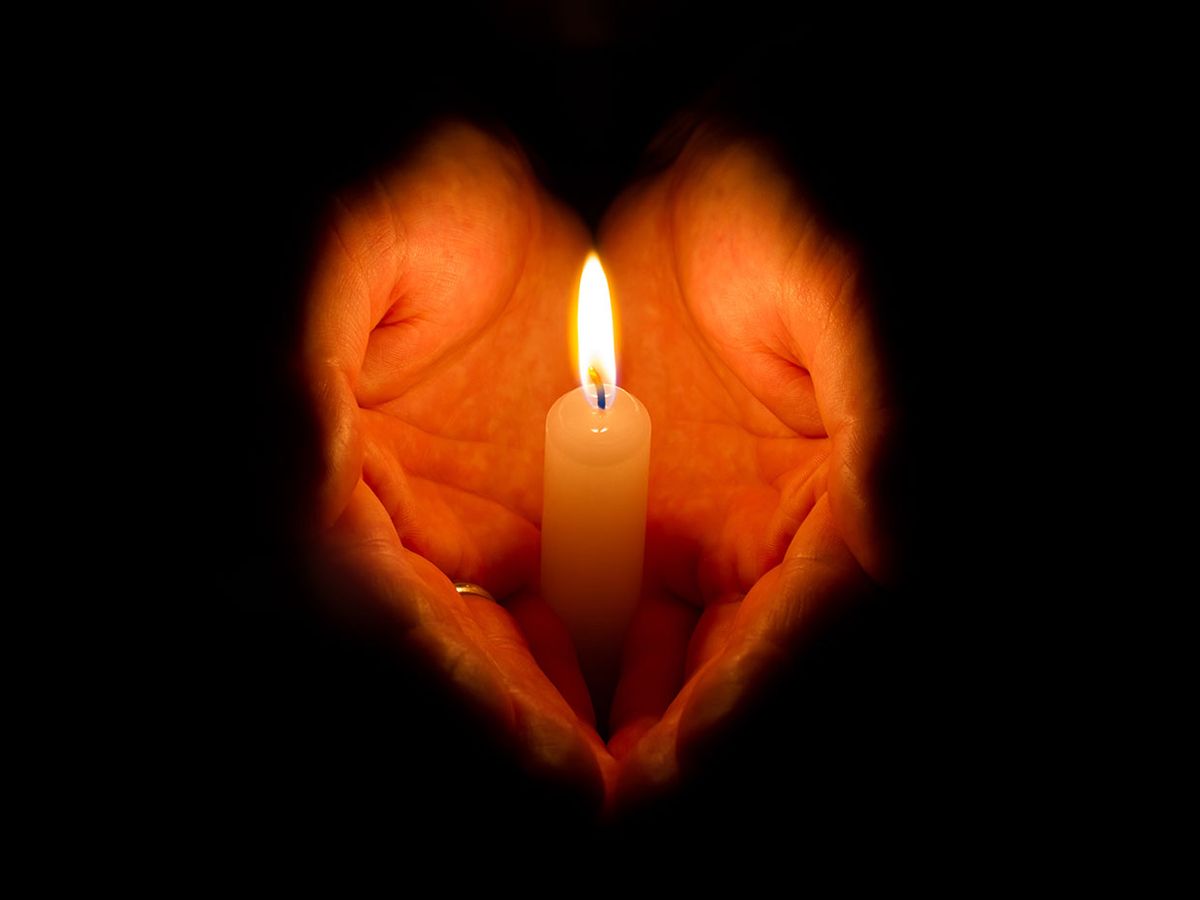 A pair of hands forming a heart shape while holding a lit candle.
