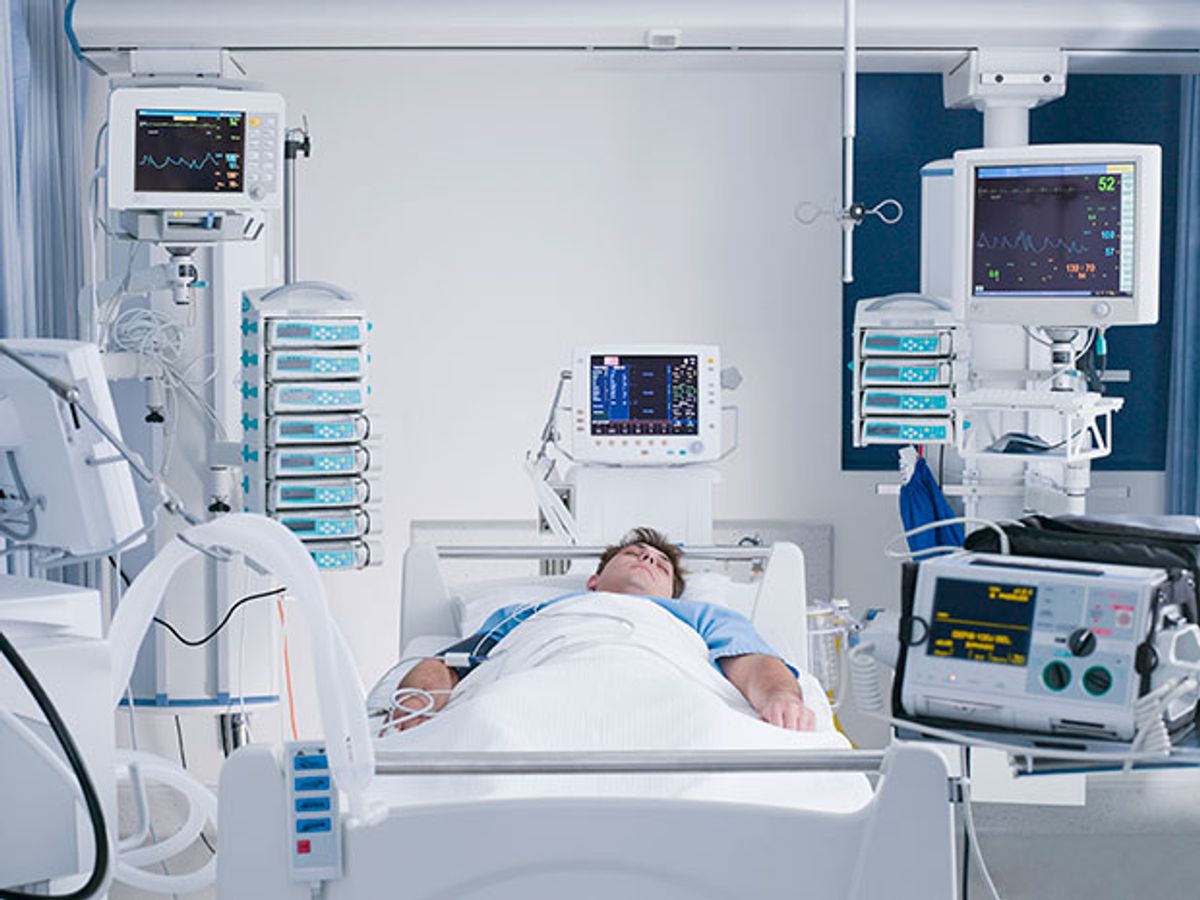 A patient lies in a hospital bed in the ICU, surrounded by machines and monitors