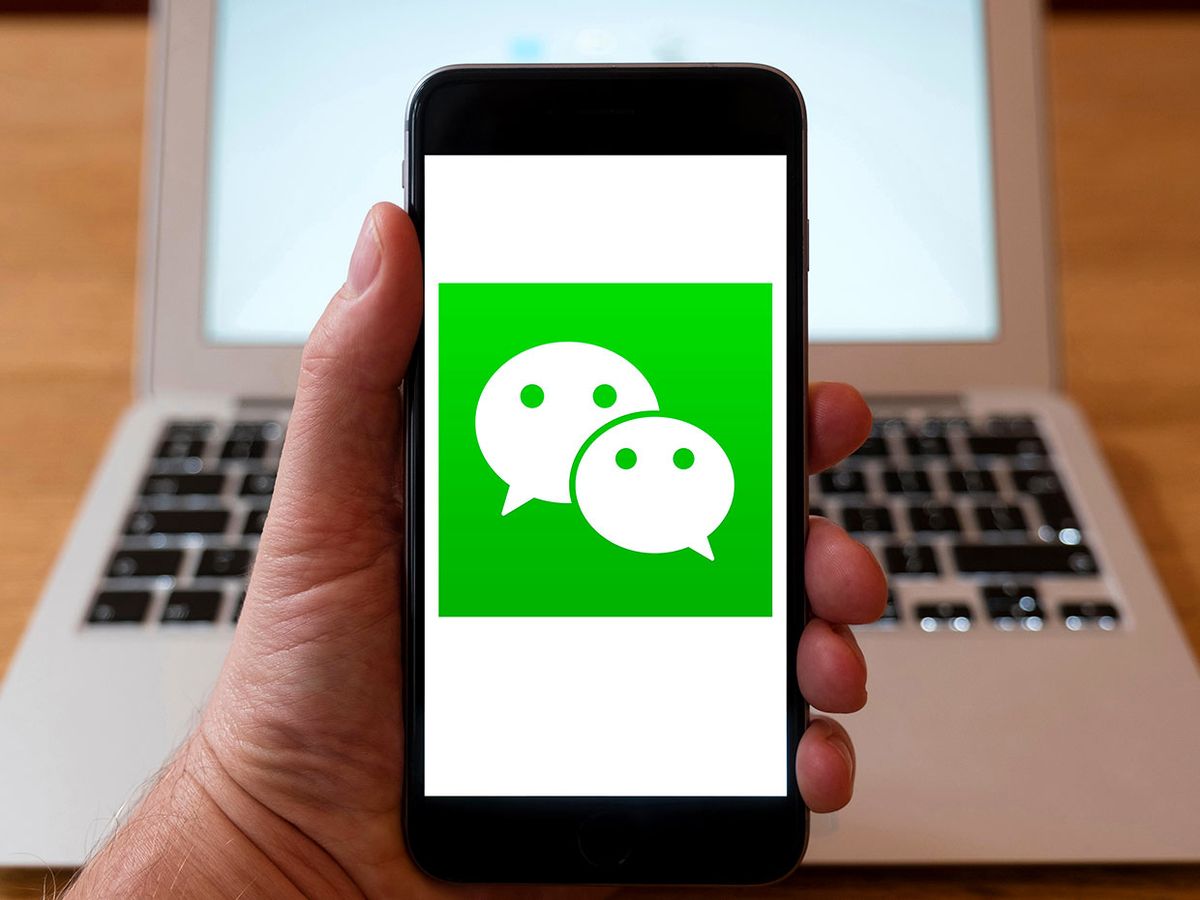 A person holds a phone up as it displays the WeChat logo.