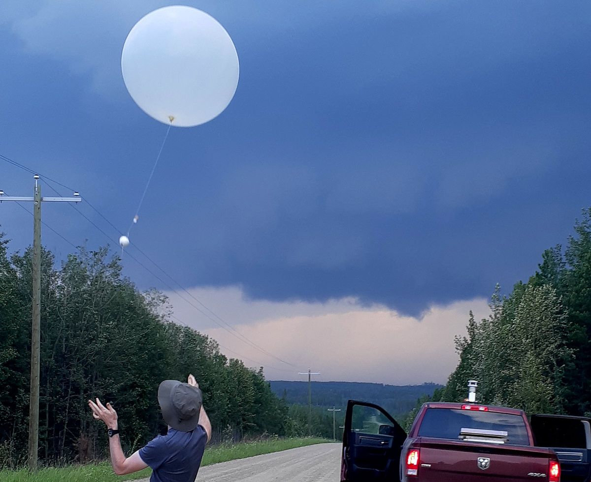 A person in a hat has just released a white balloon with a long string and white circular ball on it. A dark thundercloud looms over the scene.