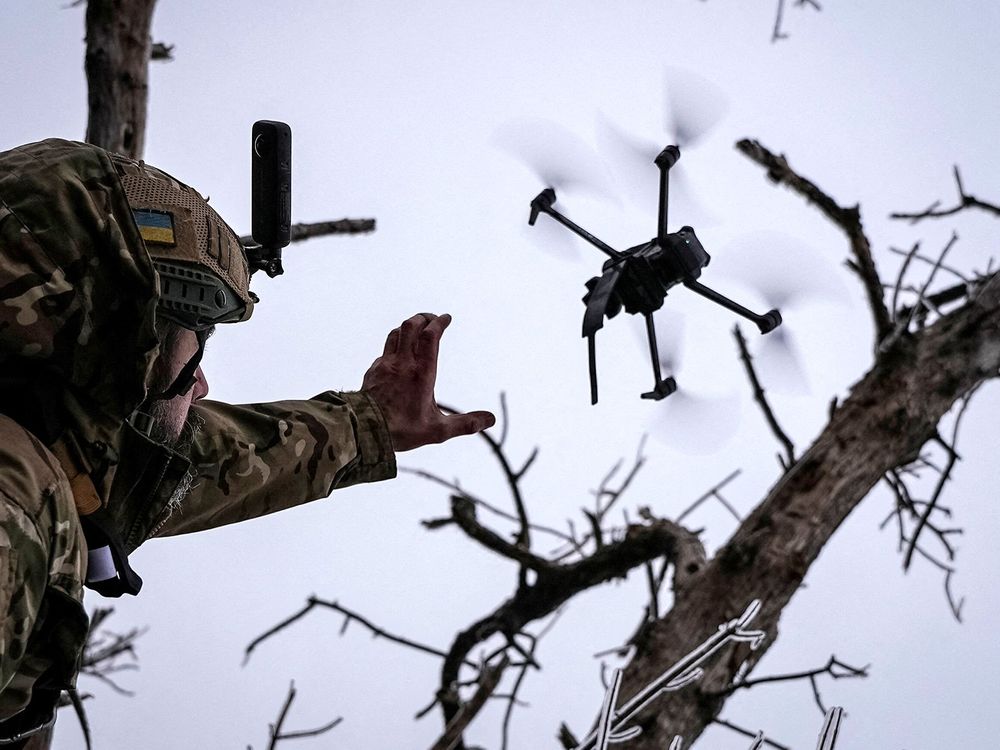 A person in military gear launches a drone skyward.
