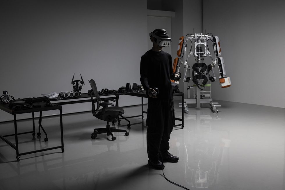 A person stands in a labratory while wearing a mixed reality headset. They're surrounded by gadgets and an exoskeleton. 