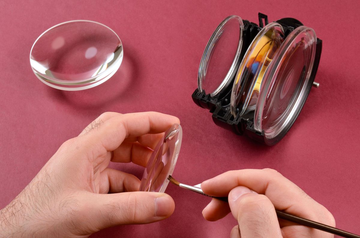 A person uses a brush to apply epoxy to a set of lenses.
