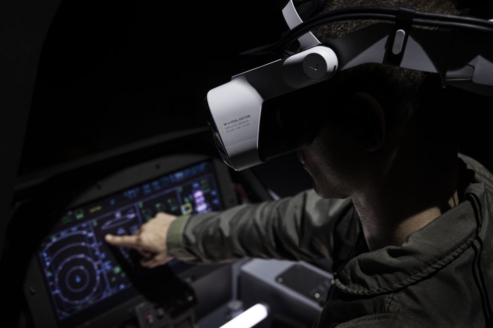 A person wearing a mixed reality headset uses a flight simulator. They lean forward in the simulated cockpit to manipulate the virtual aircraft's controls 