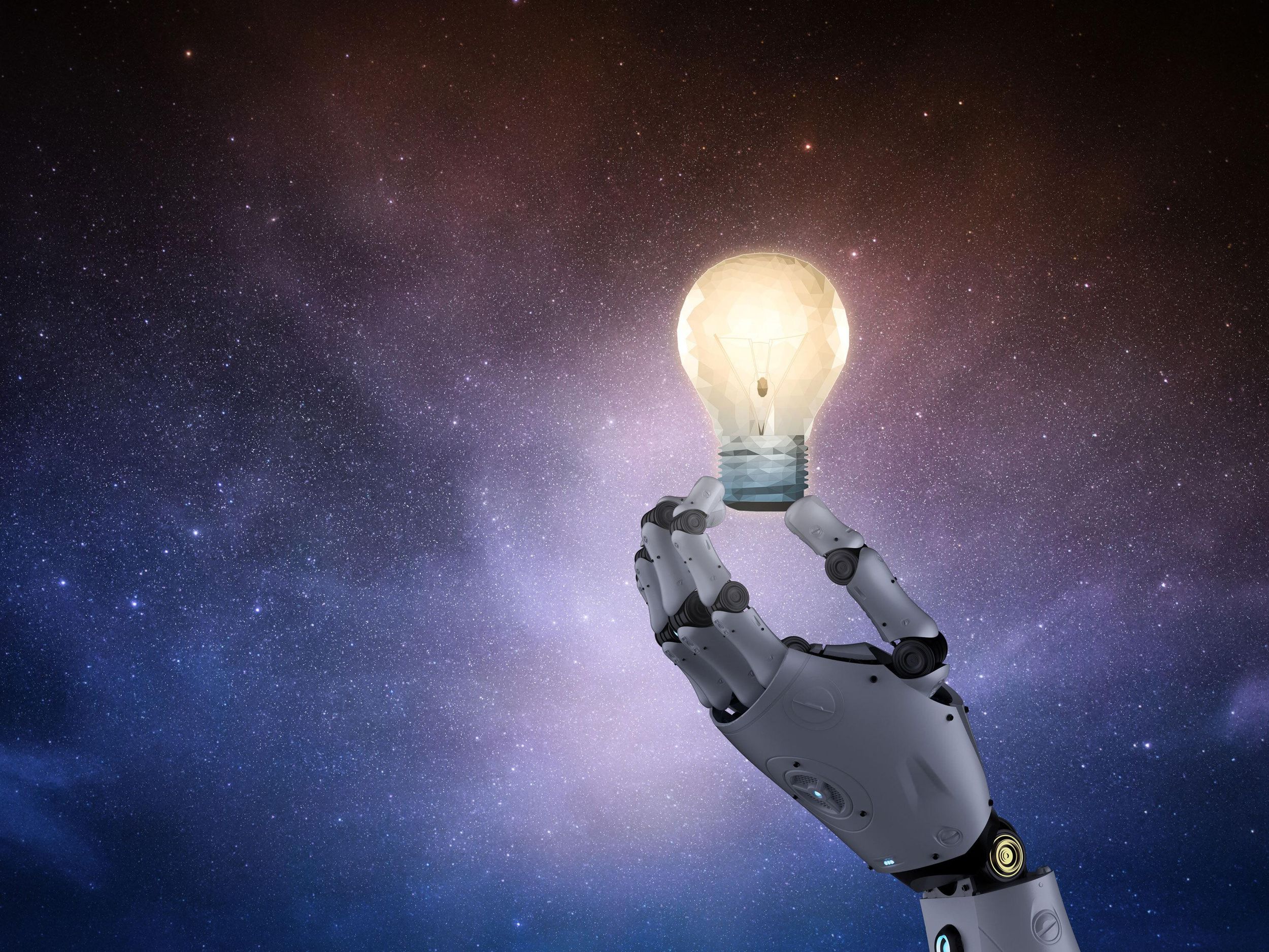 A photo-illustration of a robotic hand holding a light bulb against a starry sky. 