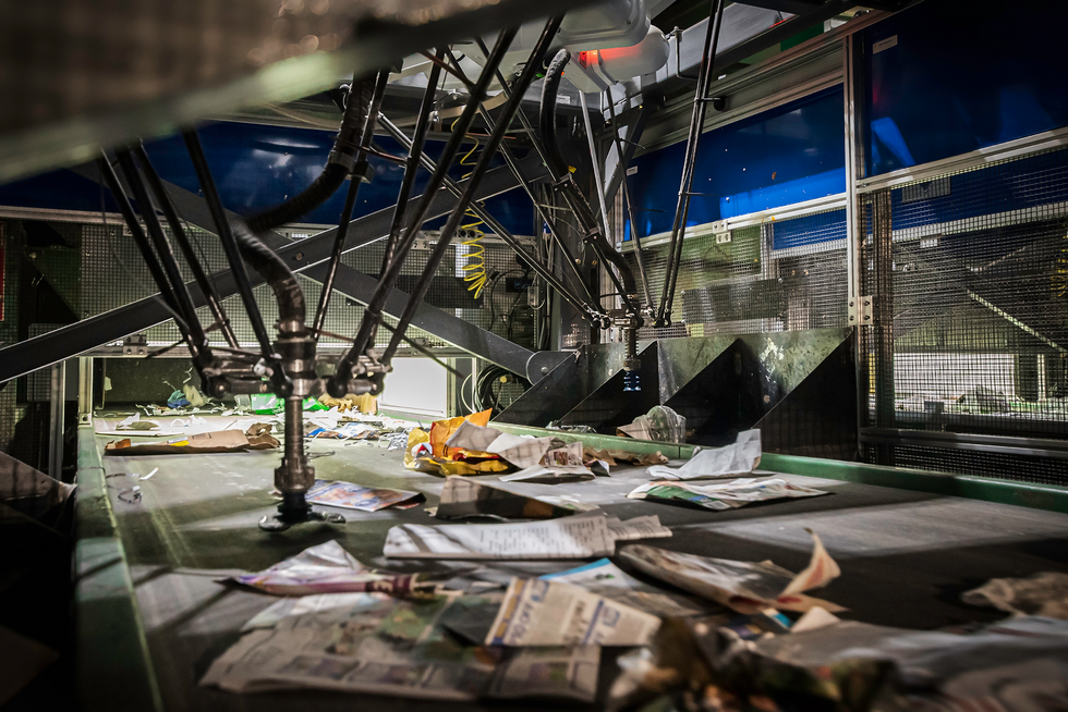 A photo of a conveyor belt with discarded paper on it and robot gripper grabbing items.