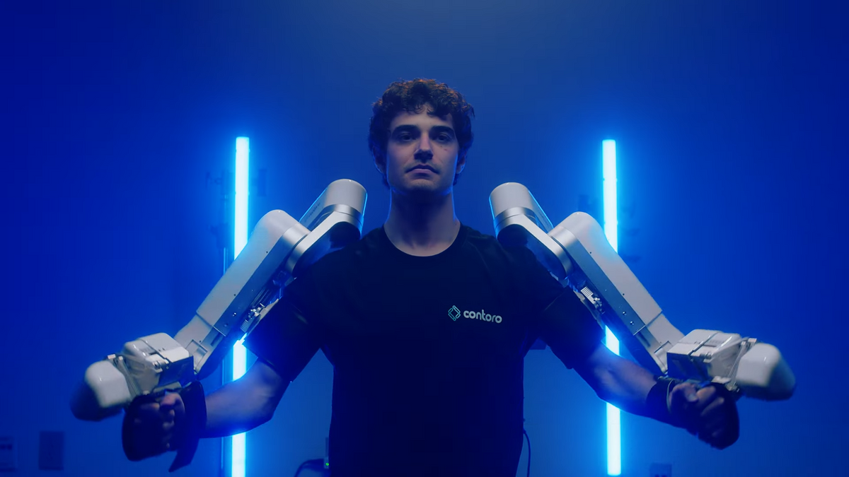 A photo of a human with two white robotic arms strapped to their arms 