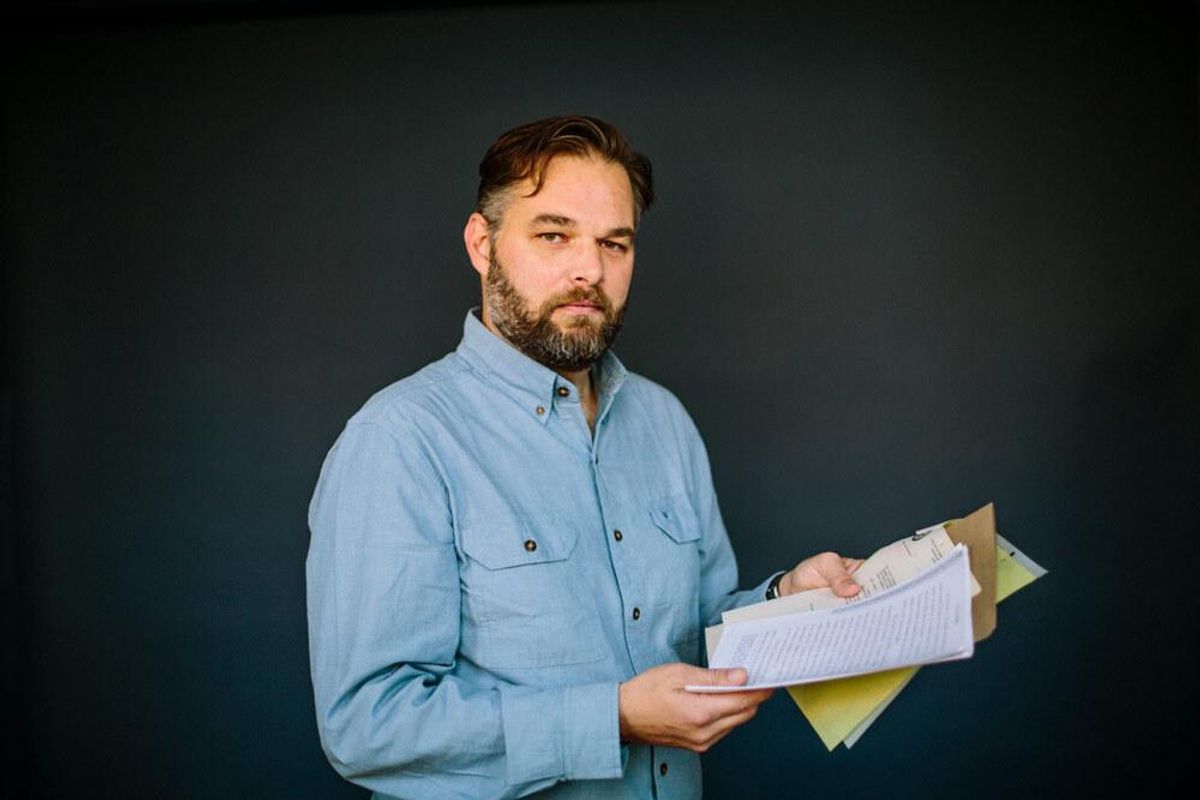 A photo of a man in a blue shirt holding folder and papers.  