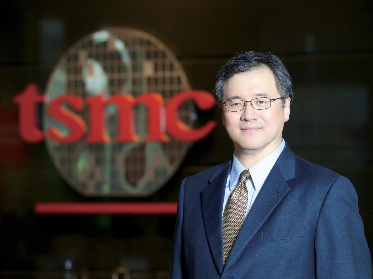 A photo of a man in a blue suit and glasses in front of a logo that says “tsmc”