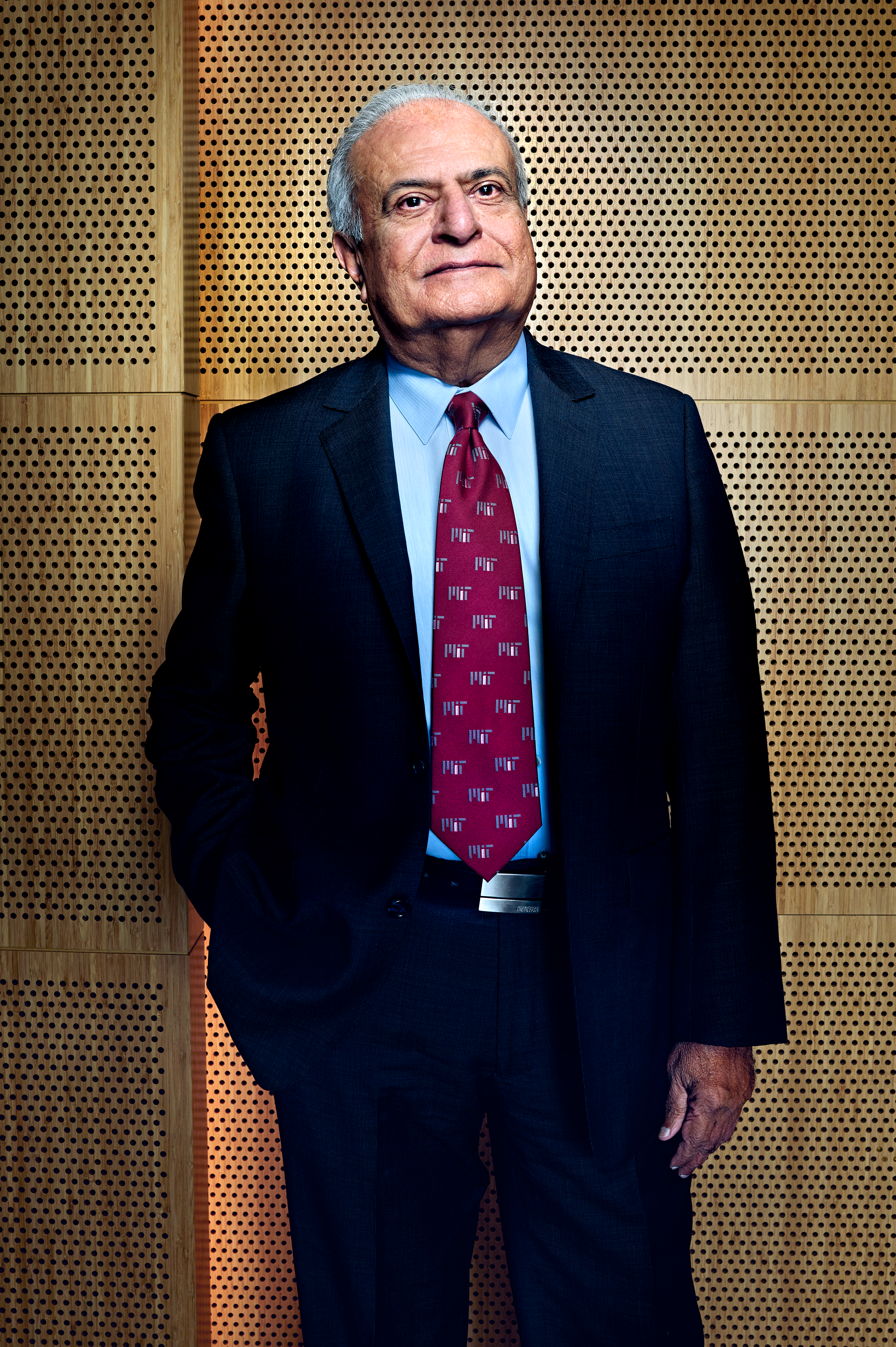 A photo of a man in a dark suit in front of a wooden background.  