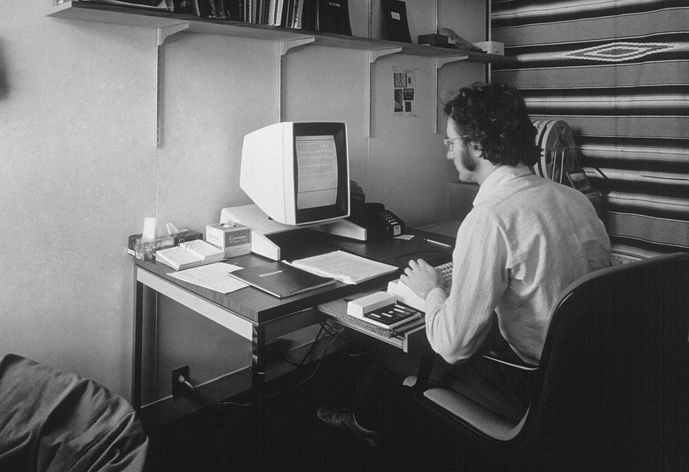 A photo of a man in an office in front of a computer.  