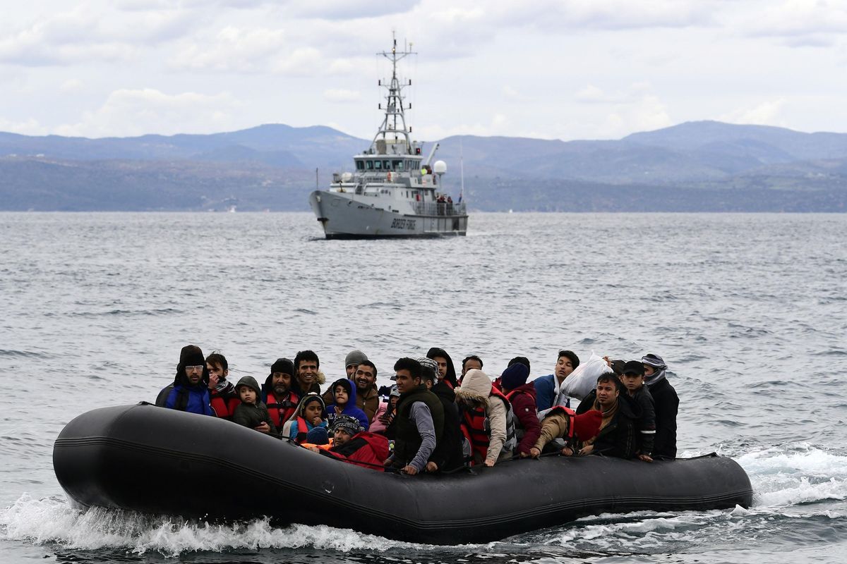 A photo of a number of people sitting in a inflatable boat on the water with a patrol ship in the background. 